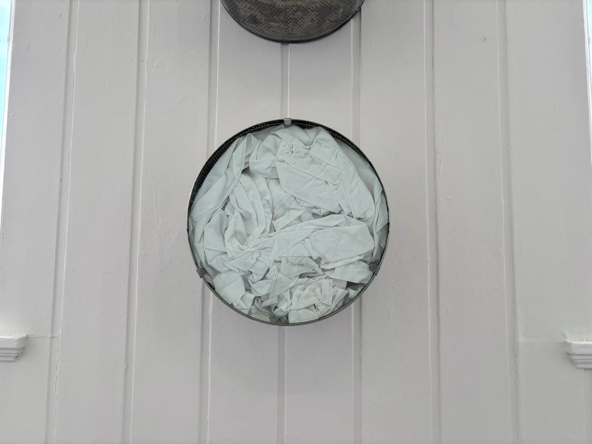 White bed sheets crammed into washing machine drum and mounted on wall