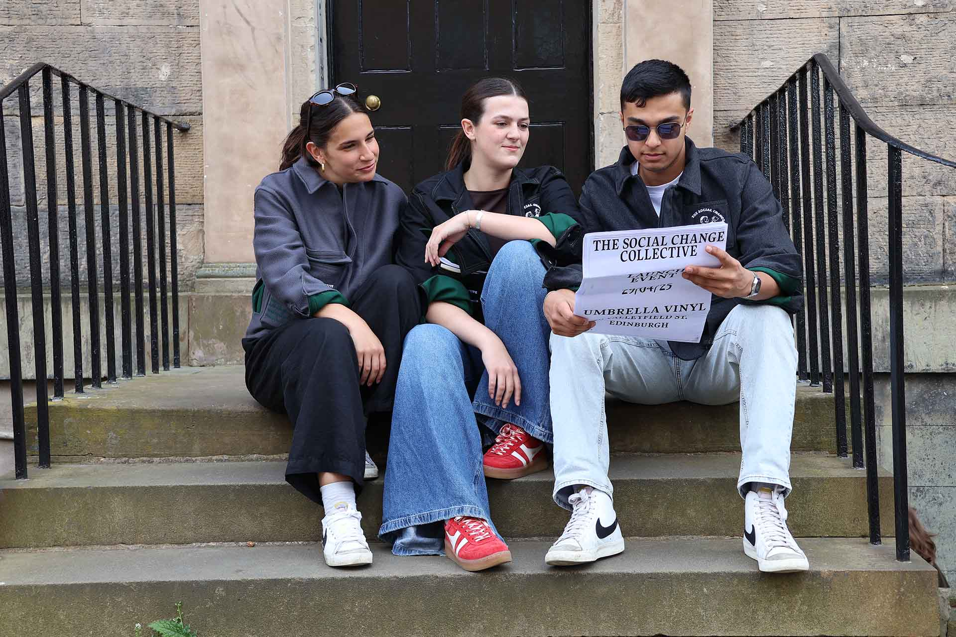 Three people sitting on steps reading newspaper