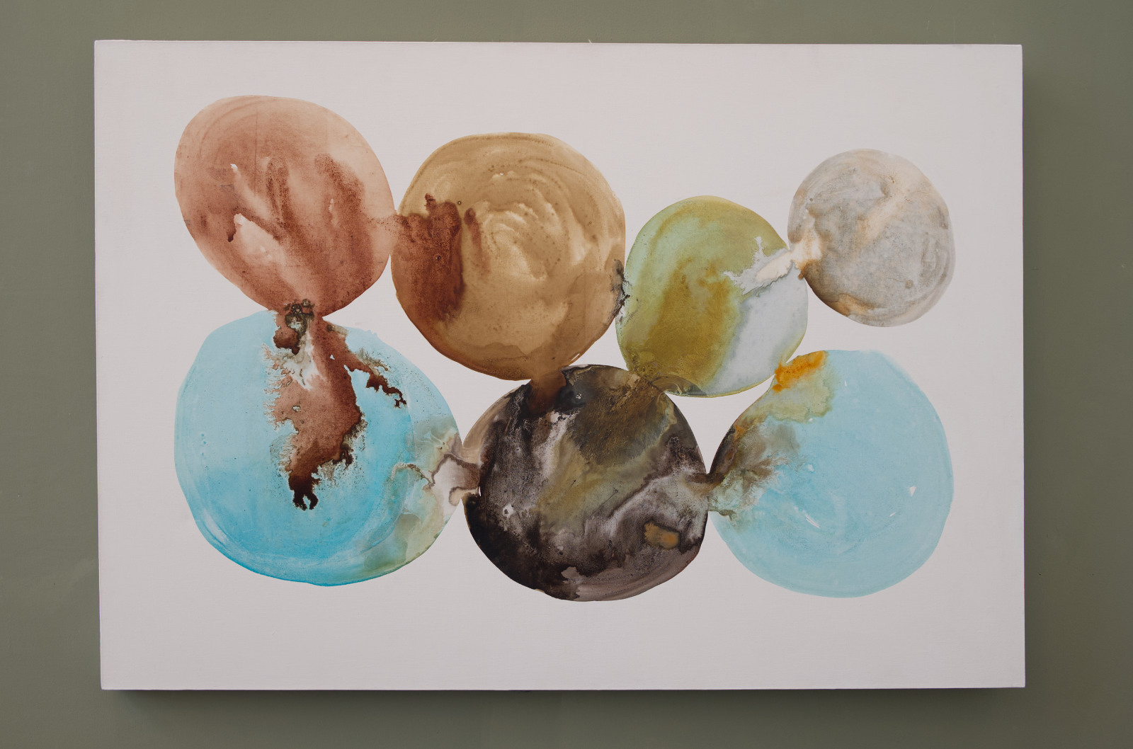 A 130 × 90 centimetre landscape-format canvas made with natural inks, showing seven rounded, overlapping pools of colour on a white ground. The forms include pale blue, rust orange, ochre, green, grey, and dark brown areas, with visible staining, bleeding, sedimentation, and crystallised edges.