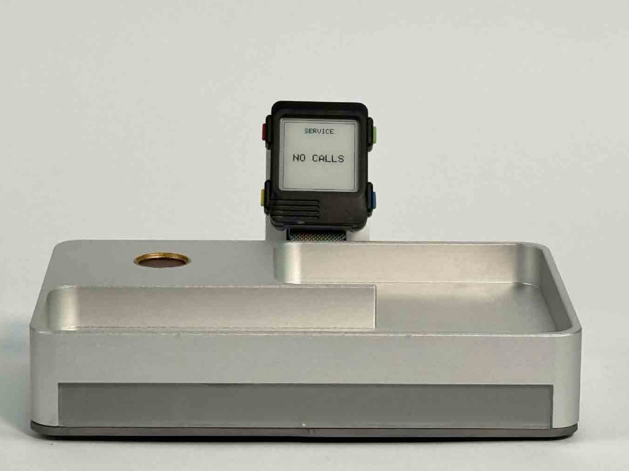 TACT aluminium tray terminal shown with the Watchy wearable displaying “NO CALLS”.